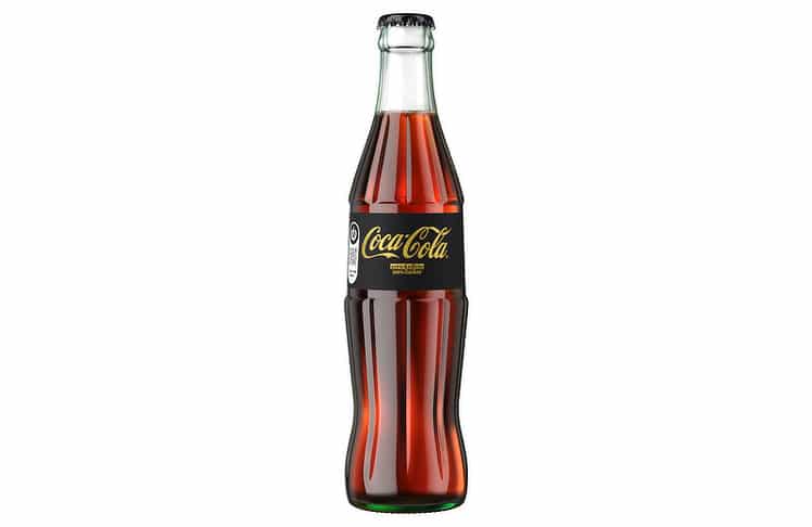 Serviert wird die Variante in einer 0,33-Liter-Mehrwegglasflasche mit schwarzem Etikett und goldener Typografie. © The Coca-Cola Company