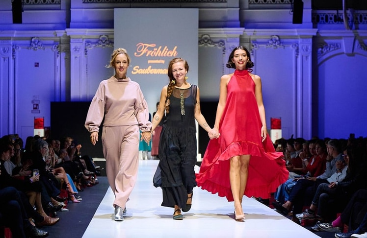 Bei Saubermacher auf der VIENNA FASHION WEEK.26 gehen Schauspielerin und Aktivistin Lilian Klebow (l.), Designerin Gabriele Rigby (M.) und ein Model (r.) gemeinsam über den Laufsteg. Das Model präsentiert eine Kreation von Rigbys Modelabel FRÖHLICH. © Saubermacher/Sabine Klimpt