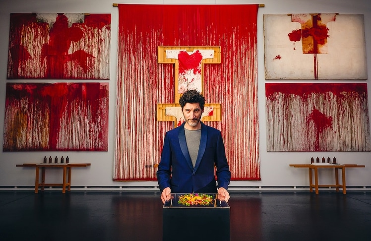 Paul Ivić, Küchenchef des Restaurants Tian, präsentiert ein farbenfrohes Gericht im Nitsch Museum Mistelbach. © Österreich Werbung/Laura Vifer; Urheber Gemälde: Hermann Nitsch